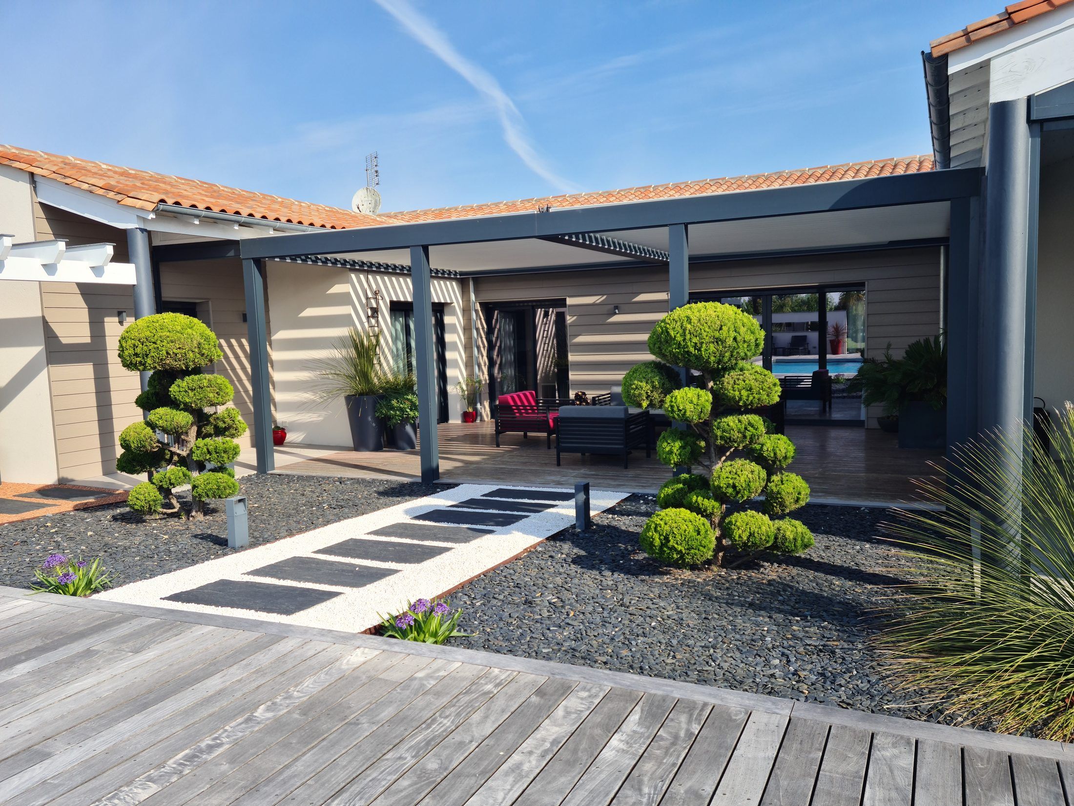 Double pergola bioclimatique aluminium anthracite sur la terrasse d’une maison contemporaine, jardin japonisant et terrasse bois, réalisation LUZ dans le pays jonzacais