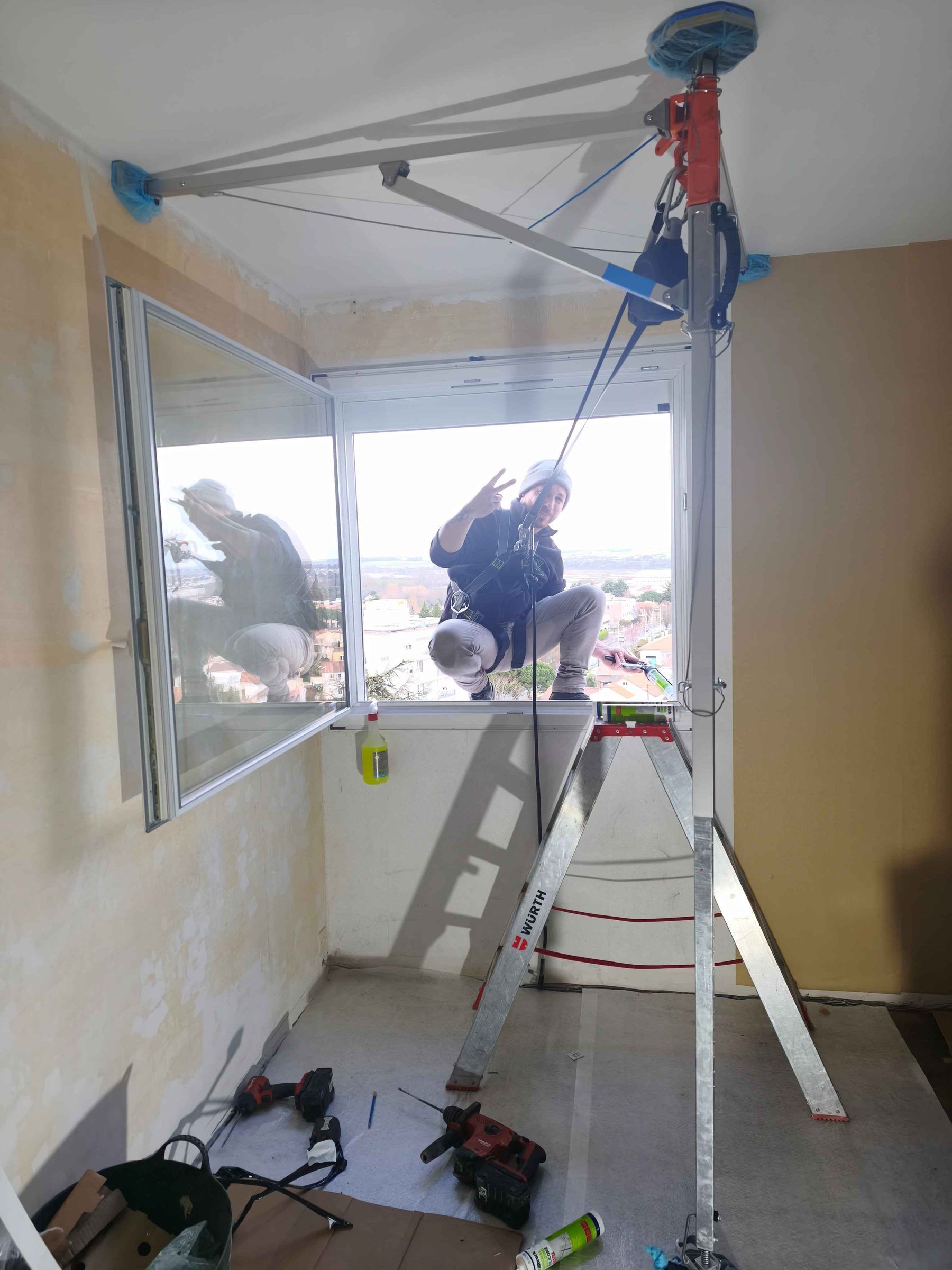 Poseur LUZ sur échelle, ligne de vie et harnais, pendant le remplacement d’une fenêtre